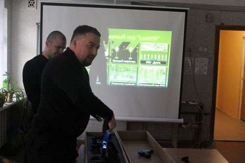 Инструктор возле экрана с тренировочными программами объясняет как работать с лазерным тиром