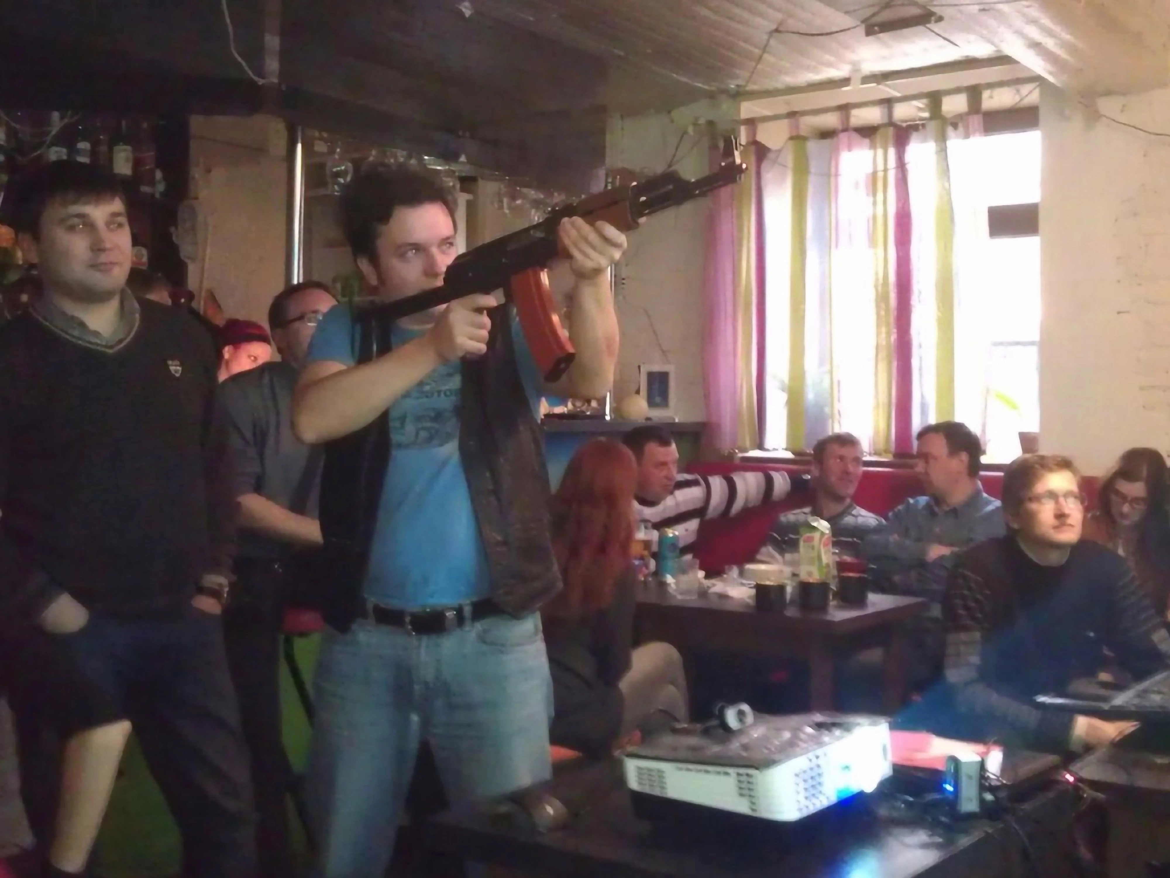 Мужчина держит игровое ружьё на фоне отдыхающих людей в ресторане с лазерным тиром